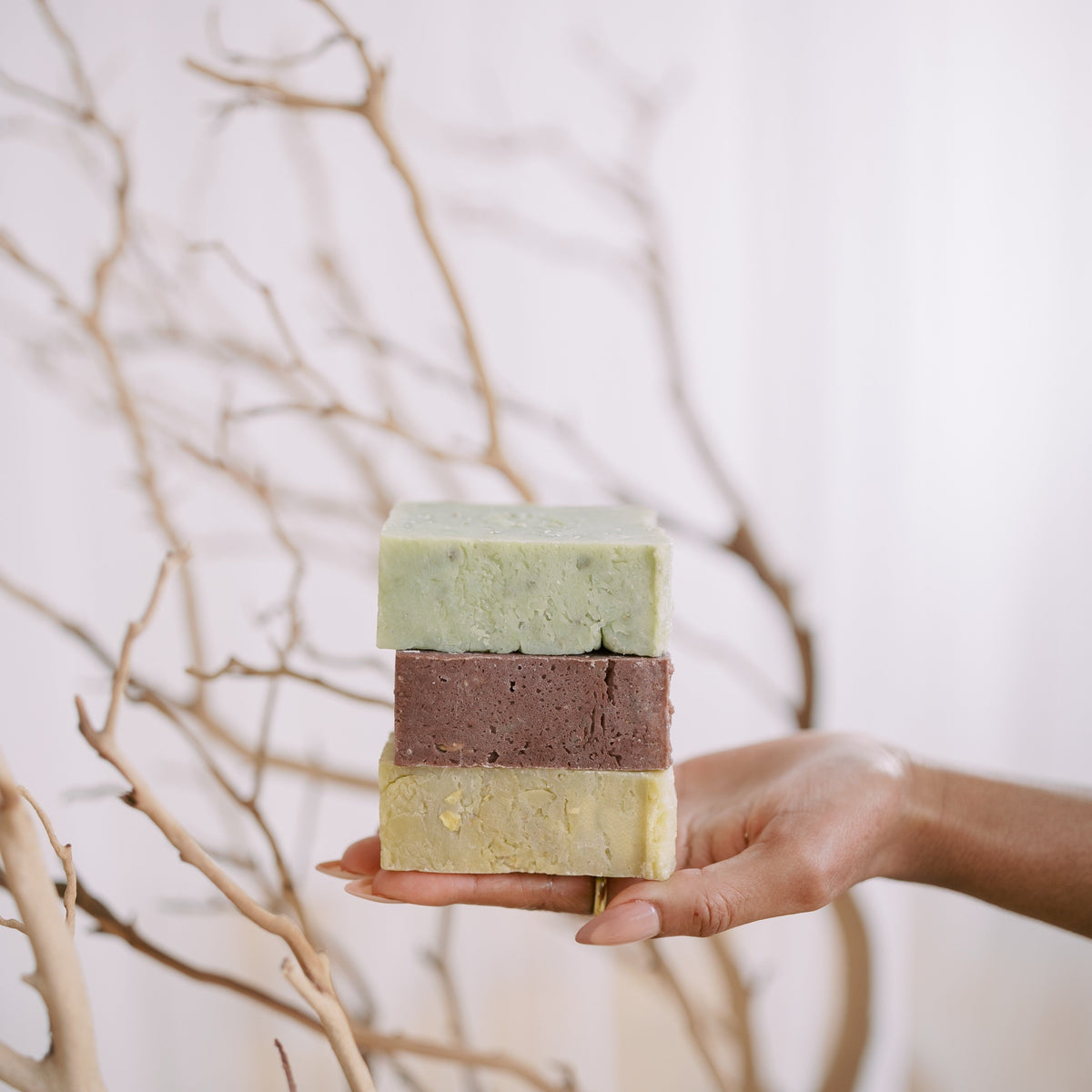 Hand holding three stacked soap bars with a neutral background