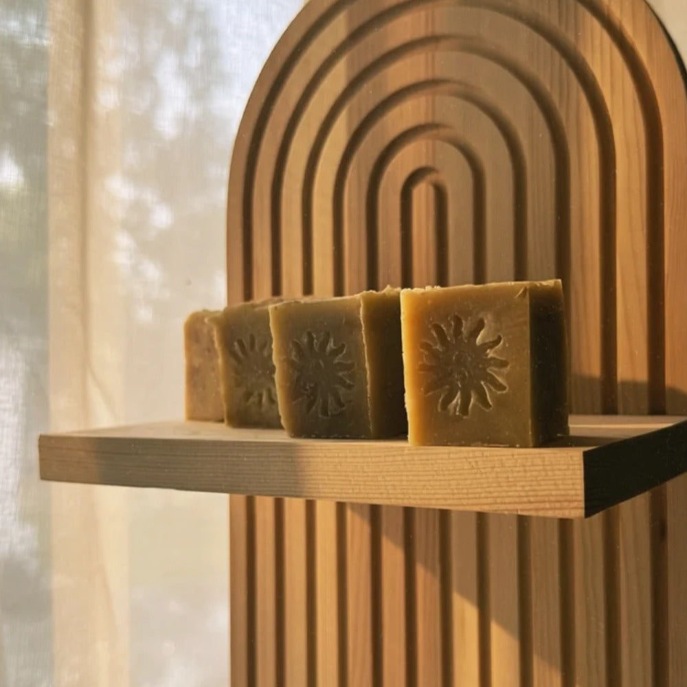 Four rectangular bars of natural yellow-green hemp soap with embossed sun ray designs, displayed on a wooden shelf in front of a wooden arch backdrop